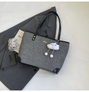 Detail of gray canvas tote bag with black leather edges and cloud plush keychain