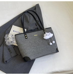 Detail of gray canvas tote bag with black leather trim, gold tag and plush cloud charm