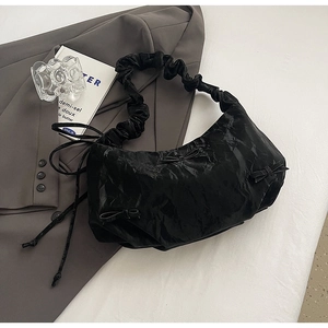 Détail du sac plissé noir avec nœuds et bandoulière nuage sur une veste grise