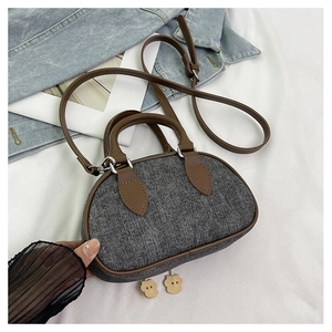 Dettaglio della borsa pillow in denim a contrasto con manici in pelle marrone e ciondoli