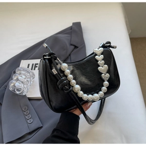 Detail view of black patent leather underarm bag with pearl and silver heart chains