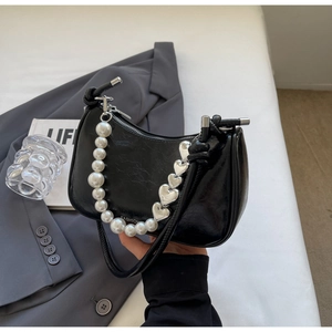 Detail of black glossy patent leather handbag with pearl and silver heart metal chains