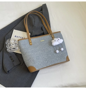 Detail of gray canvas tote bag with brown leather handles and plush cloud charm accent