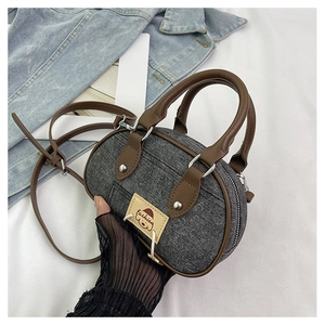 Dettaglio borsa a bauletto in denim grigio con manici in pelle marrone e patch