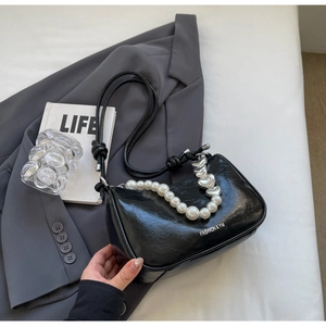 Detail of black pleated bag featuring pearl strap, heart buckle and fashion text