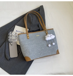 Close-up of a gray fabric tote bag with brown leather accents and a fluffy cloud pendant