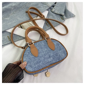 Dettaglio della borsa a tracolla in denim con finiture in pelle marrone e ciondolo decorativo