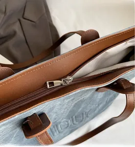 Close-up of the smooth silver zipper closure on a blue denim tote bag with brown straps