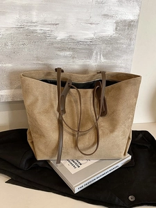 Large khaki suede tote bag with brown straps placed on fashion books for a vintage aesthetic