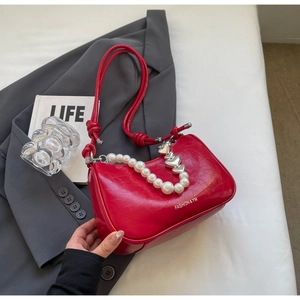 Detail of red leather shoulder bag with pearl heart chain and braided strap over a suit