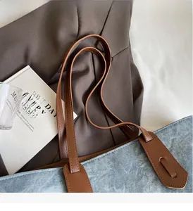 Detail of blue denim tote bag with brown leather handles and reinforced stitching