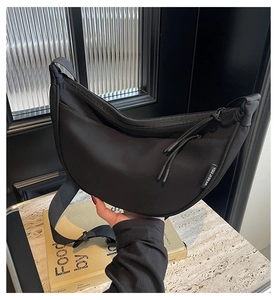 Detail of black nylon dumpling bag with adjustable strap and logo label on the side