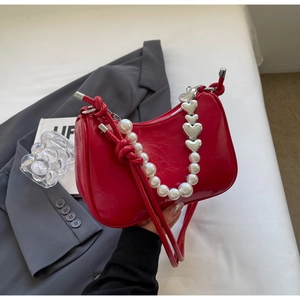 Detail of red faux leather underarm bag featuring pearl and heart chain decor