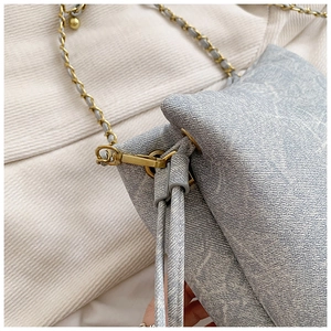 Detail of light blue denim bucket bag with golden chain strap and decorative side drawstring