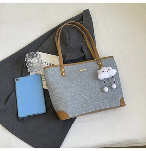 Close-up of grey fabric tote bag with brown leather handles and plush cloud charm