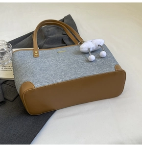 Detail of gray denim tote bag with brown leather accents and a white cloud charm