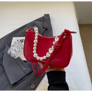 Detail of red glossy underarm bag featuring a large pearl handle and silver heart charm