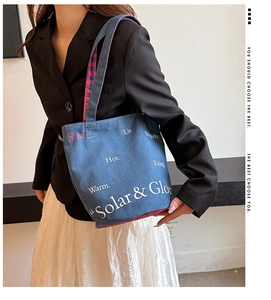 Dettaglio della borsa tote in tela con scritte artistiche su modella con blazer nero
