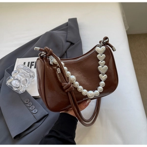 Detail of brown patent leather underarm bag with pearl strap and silver heart charm