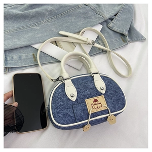 Dettaglio della mini borsa in denim con manici in pelle bianca e ciondoli orsetto