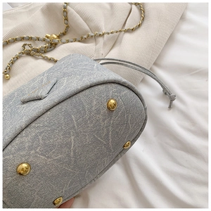 Detailed macro view of light grey bucket bag with gold anti-wear studs and fine metal chain