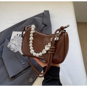 Detail of glossy brown saddle bag featuring pearl and silver heart decorative handle