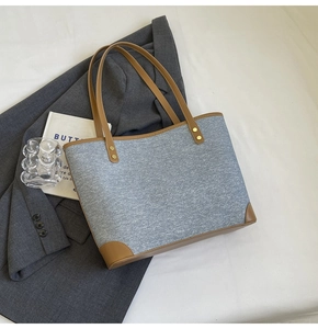 Detail of grey-blue denim tote bag with brown leather handles and metallic rivets