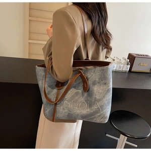 Detail of blue canvas tote bag with embossed MIDUOLA lettering and leather shoulder strap