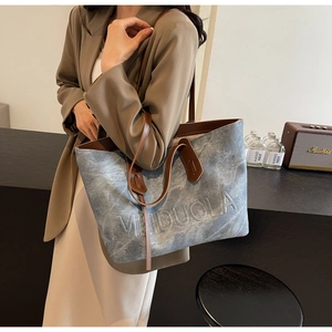 Detail of blue washed canvas tote bag with brown leather straps and embossed logo text