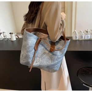Detail of blue denim texture tote bag with brown leather straps and embossed logo text