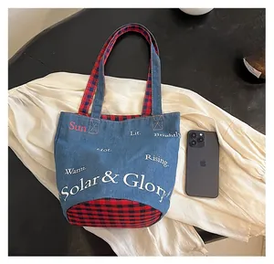 Dettaglio della borsa tote in denim con manici scozzesi e stampa accanto a un cellulare