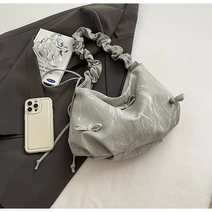Détail du sac à main plissé argenté avec texture métallique, nœud et poignée froncée