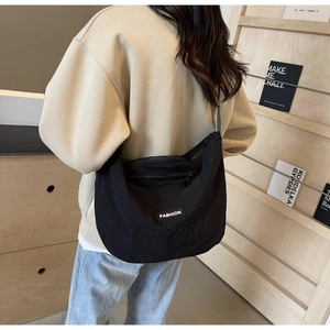 Detail view of a black nylon crescent crossbody bag worn by a model in a cozy home setting