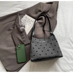 Detail view of grey polka dot tote bag with silver bow accent and black leather trim