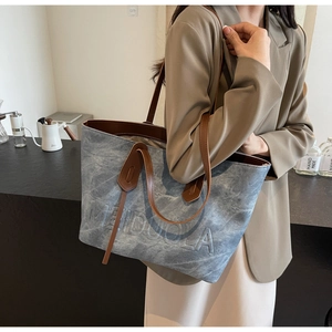 Detail of light blue textured tote bag with brown leather handles and embossed letters