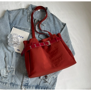 Deep red nylon tote bag with decorative leather belt and metal buckle on denim background