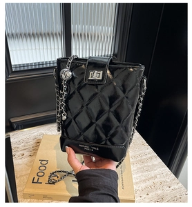 Detail of black quilted bucket bag featuring a silver chain and adjustable metal ball