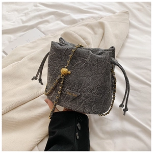 Detail of dark grey drawstring bucket bag with gold chain strap and metal ball buckle
