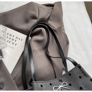 Close-up of grey herringbone bucket bag with black polka dots and silver bow detail
