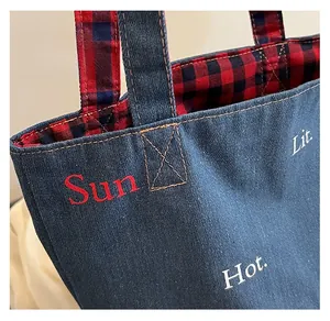 Dettaglio borsa tote in denim con fodera a quadri rossi e cuciture a contrasto