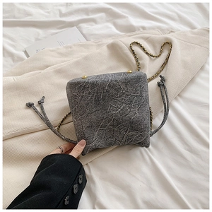 Detail of grey tweed bucket bag showing gold chain strap and drawstring closure texture