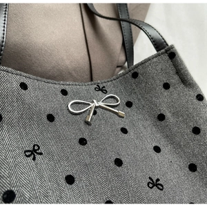 Detail of herringbone fabric with flocked dots and black embroidered bow on the tote bag