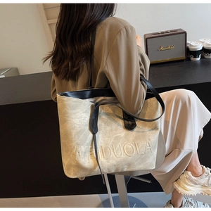 Detail of light khaki tote bag with MEIDUOLA relief text and adjustable black strap