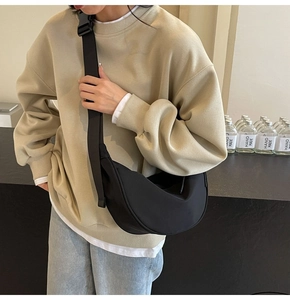 Detail of a large black nylon crescent bag with wide shoulder strap worn by a model