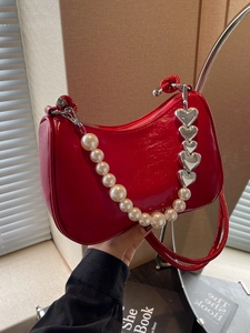 Red patent leather hobo bag with pearl chain and silver heart detail on beige background