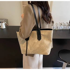 Detail of beige textured tote bag featuring embossed DUOLA lettering and black leather straps