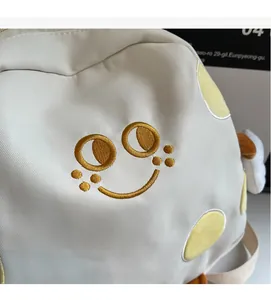 Close-up of cream canvas backpack featuring golden embroidered smiley face and plush wings