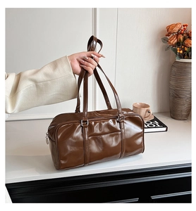 Detail of a brown glossy leather shoulder bag showing its texture and long handles