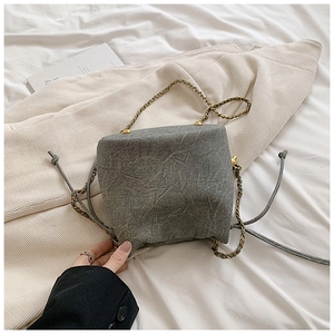 Detail of grey drawstring bucket bag with mottled texture and gold chain strap