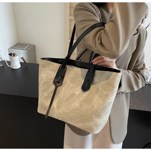Detail of beige textured tote bag featuring embossed logo and slim black shoulder straps